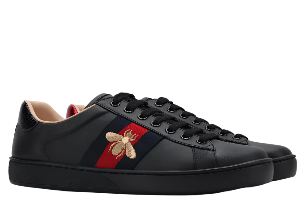 Black sneakers with a red and blue stripe and bee emblem on a light gray background